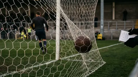 Fußball auf dem Elfmeterpunkt eines leeren Stadions, im Hintergrund unscharf das Tornetz