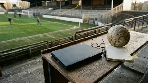 Zugeklappter Laptop und eine Lesebrille auf einem Schreibtisch neben einem Fußball, von oben fotografiert