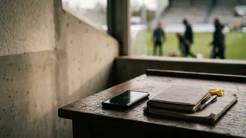 Smartphone mit dem Display nach unten neben einem geschlossenen Notizbuch und einem Stift auf einem Holztisch